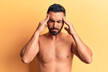 Fototapeta premium Young hispanic man standing shirtless suffering from headache desperate and stressed because pain and migraine. hands on head.