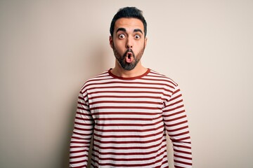 Young handsome man with beard wearing casual striped t-shirt standing over white background afraid and shocked with surprise expression, fear and excited face.