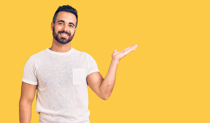 Young hispanic man wearing casual clothes smiling cheerful presenting and pointing with palm of hand looking at the camera.