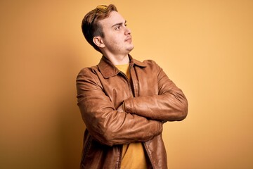 Young handsome redhead man wearing casual leather jacket over isolated yellow background looking to...