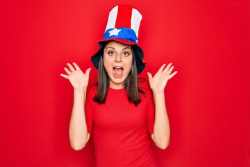 Young beautiful brunette woman wearing united states hat celebrating independence day celebrating crazy and amazed for success with arms raised and open eyes screaming excited. Winner concept