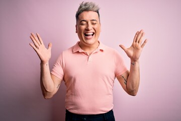Naklejka premium Young handsome modern man wearing casual pink t-shirt over isolated background celebrating mad and crazy for success with arms raised and closed eyes screaming excited. Winner concept