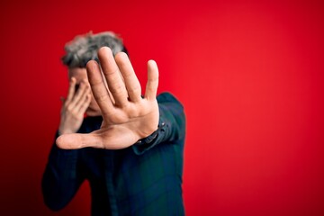 Young handsome modern man wearing elegant green shirt over red isolated background covering eyes...