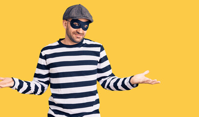Naklejka premium Young handsome man wearing burglar mask smiling showing both hands open palms, presenting and advertising comparison and balance