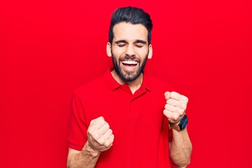 Young handsome man with beard wearing casual polo celebrating surprised and amazed for success with arms raised and eyes closed