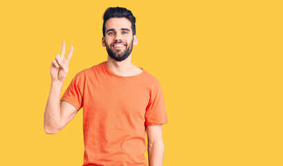 Young handsome man with beard wearing casual t-shirt smiling looking to the camera showing fingers doing victory sign. number two.