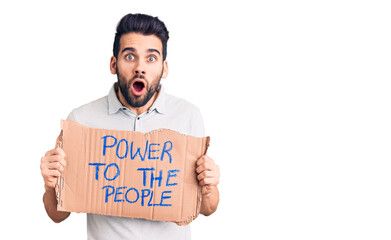 Young handsome man with beard holding power to the people cardboard banner scared and amazed with...