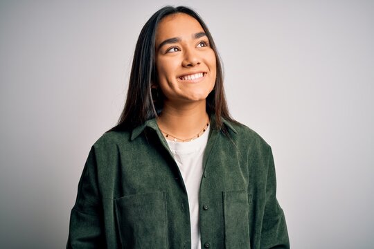 Young beautiful asian woman wearing casual shirt standing over isolated white background looking away to side with smile on face, natural expression. Laughing confident.