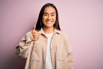 Young beautiful asian woman wearing casual shirt standing over pink background doing happy thumbs up gesture with hand. Approving expression looking at the camera showing success.