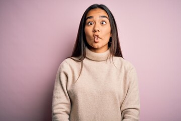 Young beautiful asian woman wearing casual turtleneck sweater over pink background making fish face with lips, crazy and comical gesture. Funny expression.