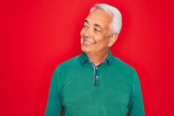 Middle age senior grey-haired man wearing casual sweater over red isoalted background looking away to side with smile on face, natural expression. Laughing confident.