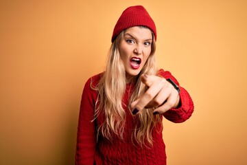 Young beautiful blonde woman wearing casual sweater and wool cap over white background pointing displeased and frustrated to the camera, angry and furious with you