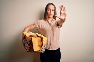 Young beautiful woman doing domestic chores holding wicker basket with clothes with open hand doing stop sign with serious and confident expression, defense gesture
