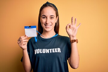 Young beautiful woman wearing volunteer t-shirt doing volunteering holding id pass card doing ok...