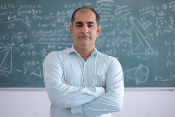 Portrait of male indian math teacher standing against blackboard, education knowledge concept.