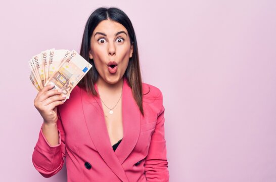 Young beautiful businesswoman holding euros banknotes over isolated pink background scared and amazed with open mouth for surprise, disbelief face