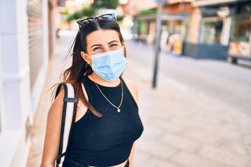 Young beautiful brunette woman wearing medical mask. Walking at town street