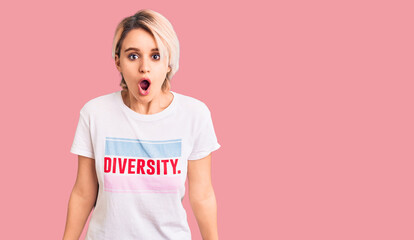 Young beautiful blonde woman wearing t shirt with diversity word message scared and amazed with...