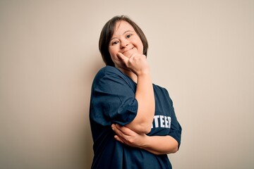 Young down syndrome volunteer woman wearing social care charity t-shirt with hand on chin thinking...
