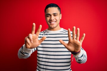 Young brazilian man wearing casual striped t-shirt standing over isolated red background showing and pointing up with fingers number eight while smiling confident and happy.