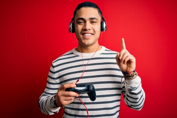 Young brazilian gamer man playing video game using joystick and headphones surprised with an idea or question pointing finger with happy face, number one © Krakenimages.com