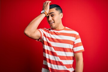 Young brazilian man wearing casual striped t-shirt standing over isolated red background surprised...