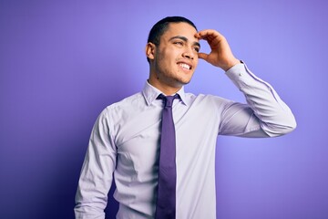 Young brazilian businessman wearing elegant tie standing over isolated purple background smiling confident touching hair with hand up gesture, posing attractive and fashionable