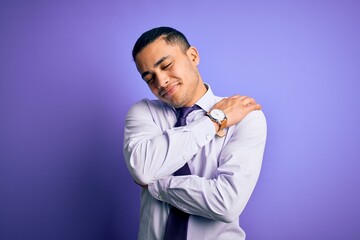 Young brazilian businessman wearing elegant tie standing over isolated purple background Hugging oneself happy and positive, smiling confident. Self love and self care