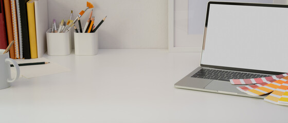 Designer home office desk with mock-up laptop, painting tools, supplies and copy space