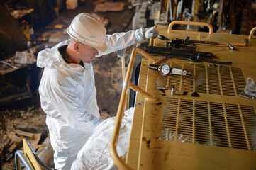 A mechanic in a white jumpsuit and helmet repairs the loader.