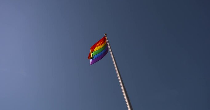 Pride Flag flying against a blue sky background in slow motion.