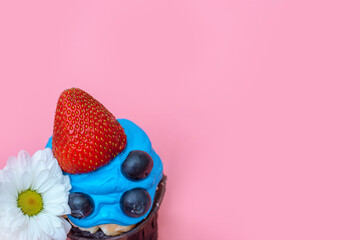 one delicious cupcake with blue cheerful cream and blueberries and strawberries for the holiday decorated with daisies on a pink background top view