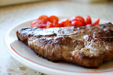 grilled juicy pork meat steak with vegetables cherry tomatoes con a white plate