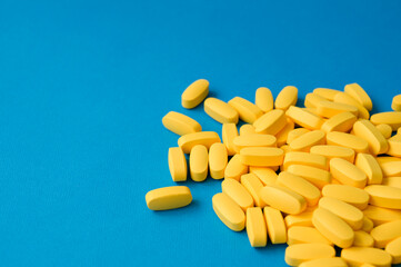 medical industry concept of yellow vitamine drug tablets lying on blue pharmacy surface with copy space