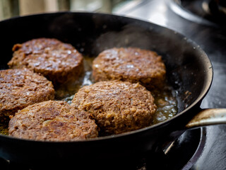 Beef burgers fried in frying pan.