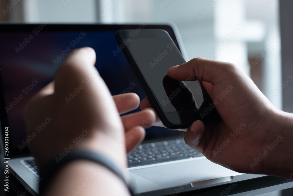 Poster mockup of man using mobile smart phone and working on laptop computer in office