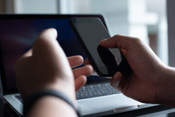 Mockup of man using mobile smart phone and working on laptop computer in office