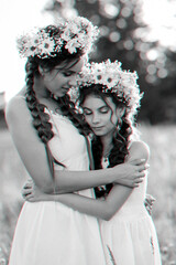 happy sisters in white dresses with floral wreaths and boho style braids in summer in a field