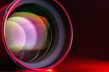 .The camera lens and the beautiful light red color. Close-up of the camera lens on a black background with red illumination. Optics.