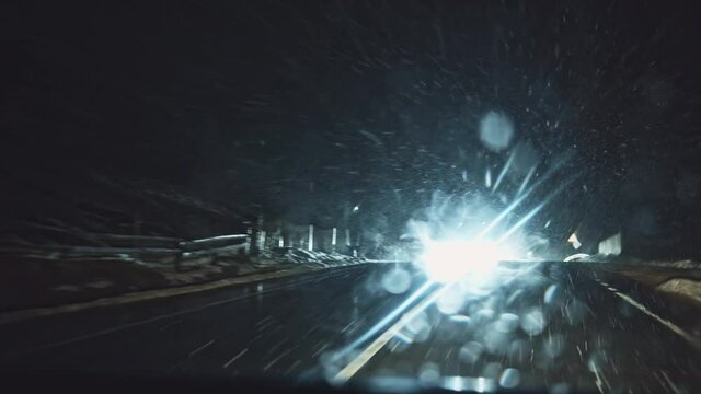 Front window car motion view of night snowstorm in the countryside. Driving on wet country road during blizzard. Wipers cleaning windows. Roadtrip.