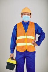 Portrait of handyman in hardhat, vest and medical mask carrying toolbox