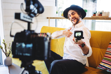Handsome casual man sitting on the couch and filming video blog. Using big and small cameras