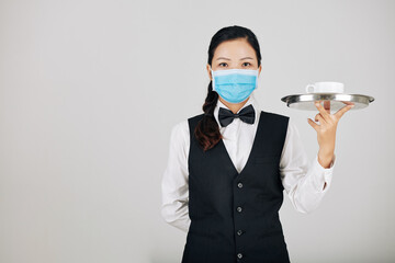 Portrait of serious yuong waitress in medical mask carrying tray with bowl of soup