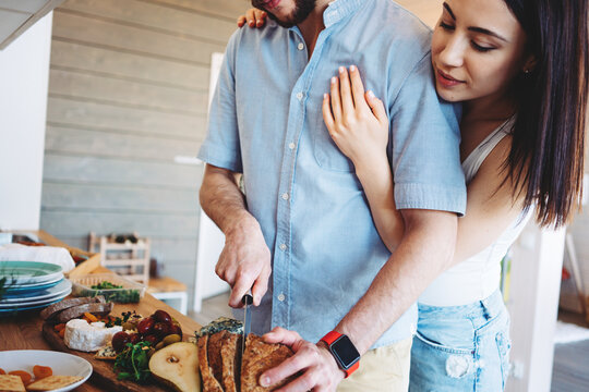 Romantic couple on the kitchen preparing food together. Hugging and cutting bread