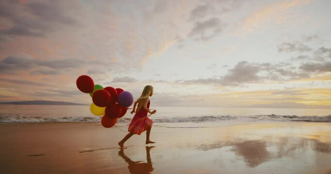 Happy young girl playing on the beach with balloons at sunset, freedom summer lifestyle concept