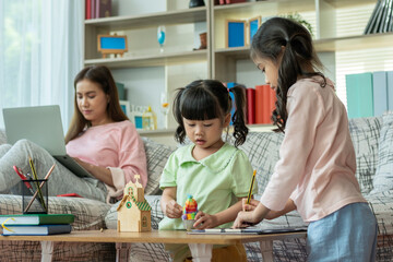 A Beautiful Asian mother busy working while looking after and teaching her children on a laptop computer at home