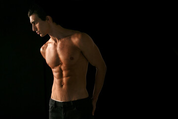 Fototapeta premium Profile portrait of a young man with shirtless torso with tanned skin, over black background. Space for text.