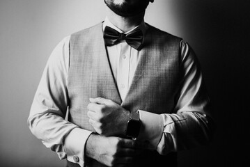 Horizontal grayscale shot of a groom in a vest and a bow getting dressed for his wedding day