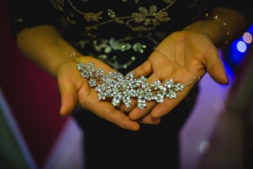 Horizontal shot of a female holding a shiny silver flowered brooch on a blurred background
