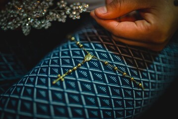 Horizontal shot of a golden bracelet with a tiny cross on a blue fabric with a silver brooch